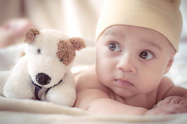 empathy - cute baby on bed with dog doll.