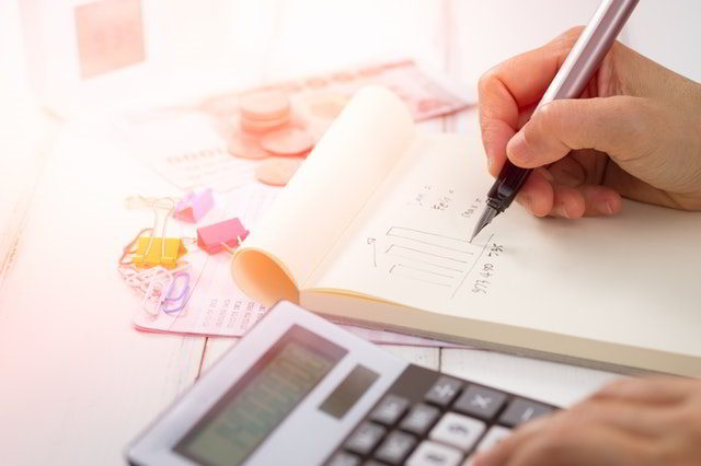 Teacher salary - man's hand drawing charts on notebook with calculator.