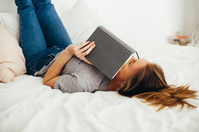 Woman reading book lying on bed.