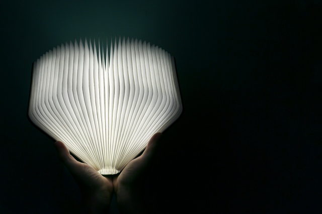 Pair of hands holding open glowing book in the dark.