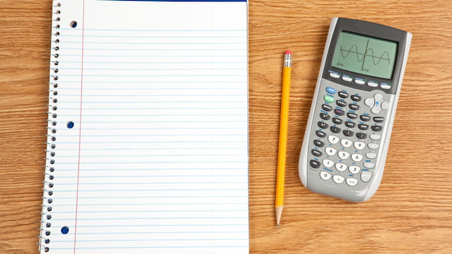 Graphing calculator with a pencil and lined notebook on a wooden desk, showcasing tools for math or science studies.